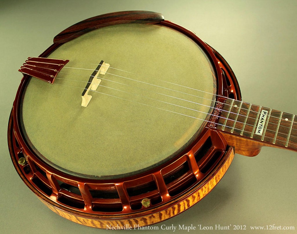 Based closely on the banjo made for Leon Hunt, this beautiful example of the Nechville Phantom Curly Maple Leon Hunt Banjo features curly maple and cocobolo.  The wooden tone ring combined with a mix of steel and nylon ball bearings gives the warm, fat tone of the famous Nechville 'Zeus' model.  The attractive honey amber on the metal components is a limited run finish.